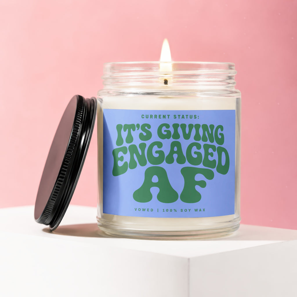 Glass candle with lit wick and "IT'S GIVING ENGAGED AF" text.
