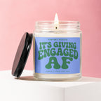Glass candle with lit wick and "IT'S GIVING ENGAGED AF" text.