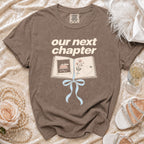 Brown t-shirt with "our next chapter" text and open book graphic.
