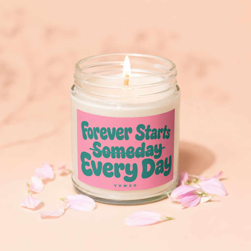 Lit candle with pink label that reads "Forever Starts Someday Every Day VOWED".