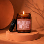 Amber jar candle with lit flame, label reads "The Adventure Begins".