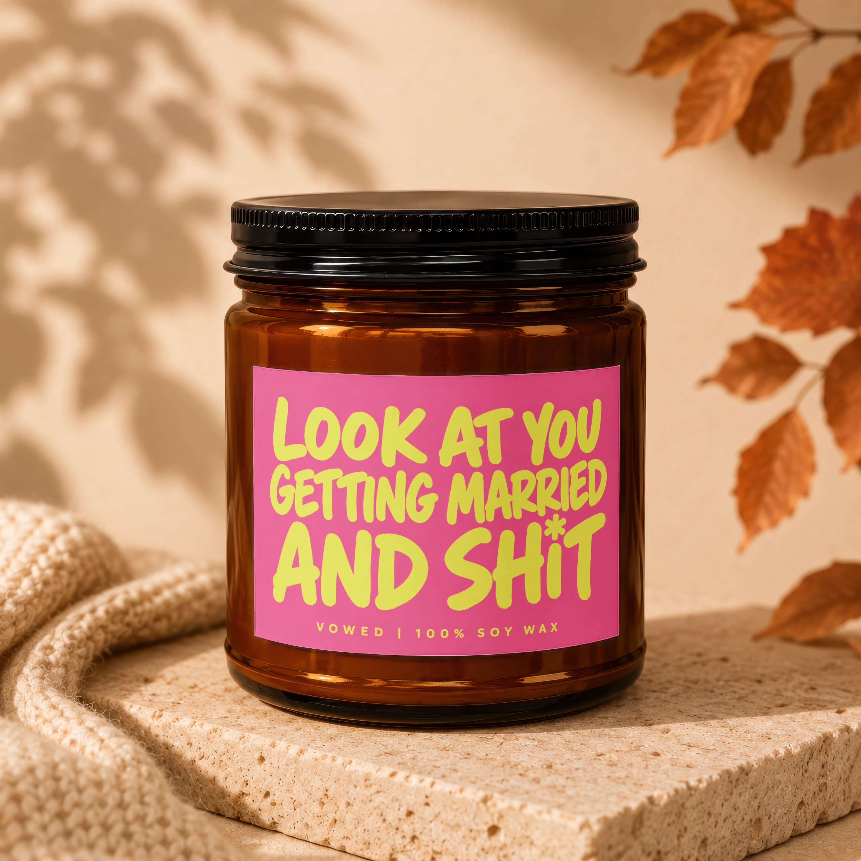 Glass candle with pink label reading "Look at you getting married and shit."