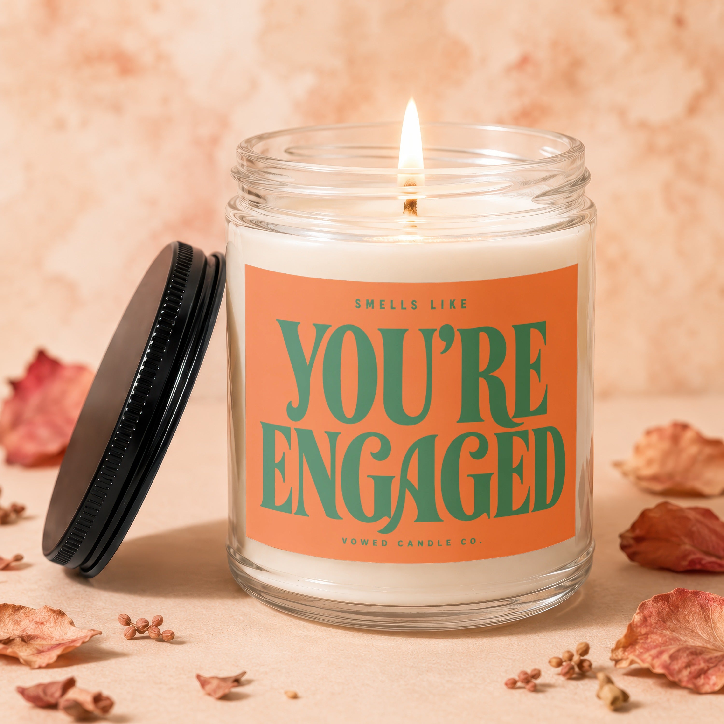Burning candle in glass jar with orange label reading "You're Engaged"