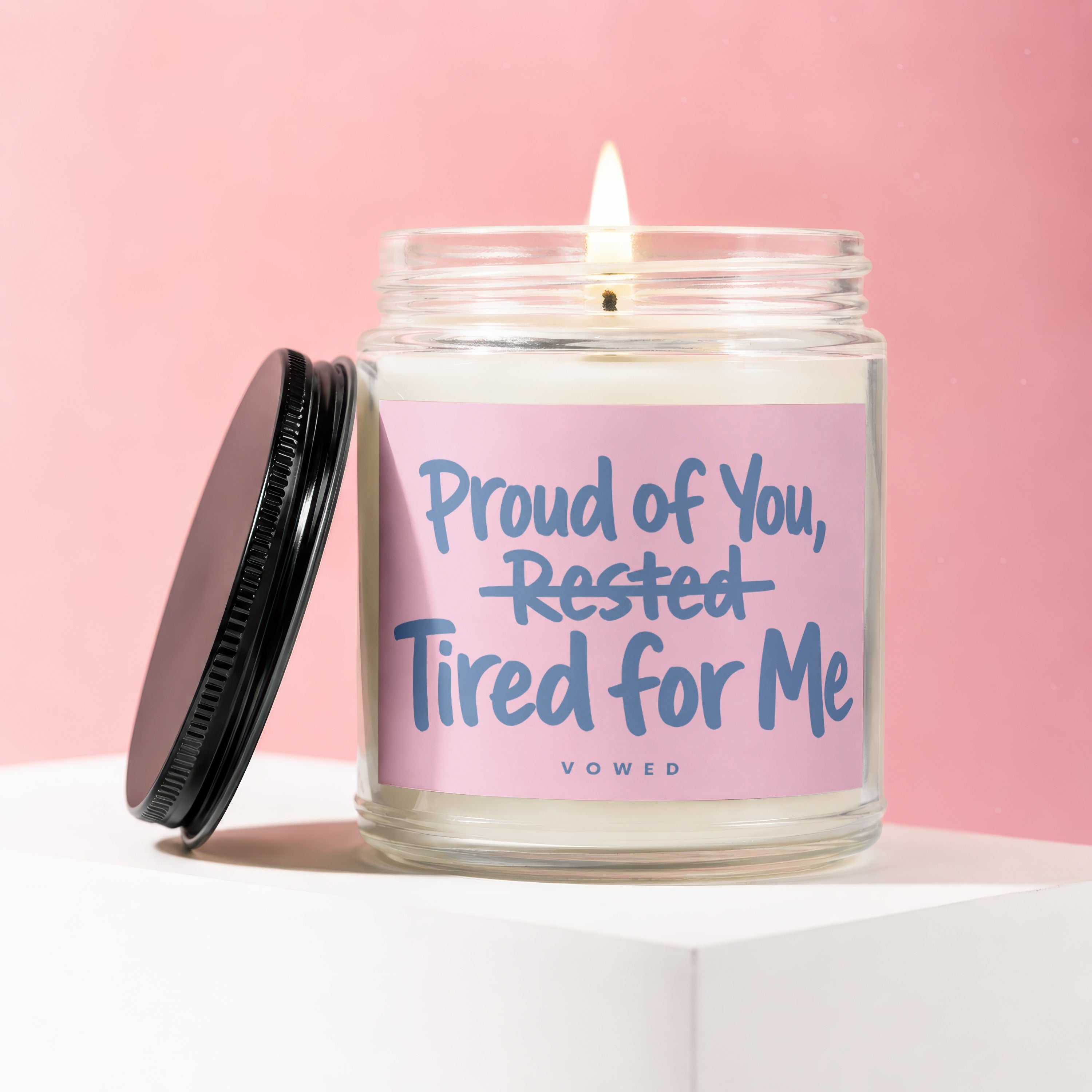 Glass candle with pink label that reads "Proud of You, Rested Tired for Me."