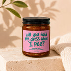Candle with pink label reading "will you hold my dress while I pee?"