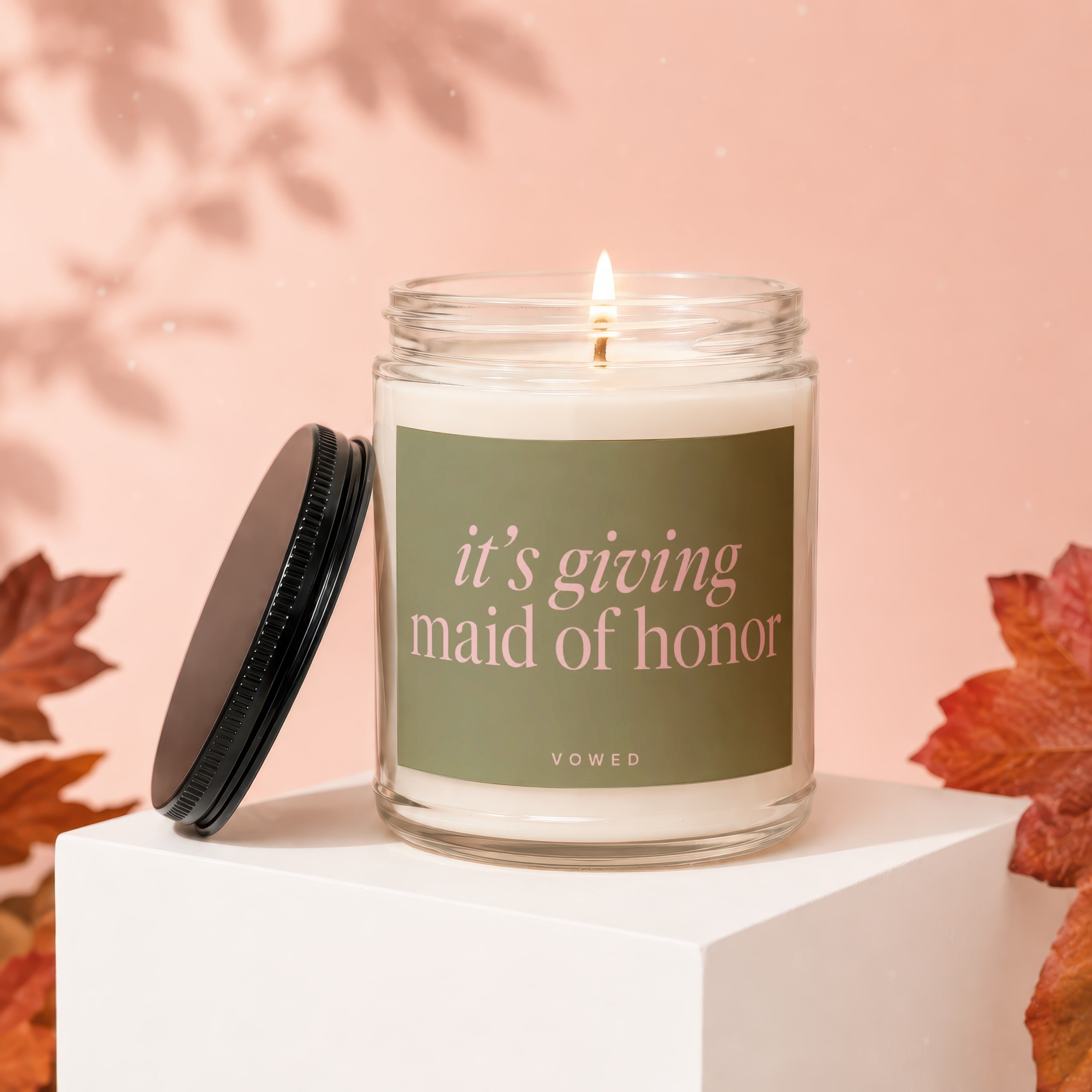 Glass jar candle with pink text "it's giving maid of honor" and brand "VOWED".