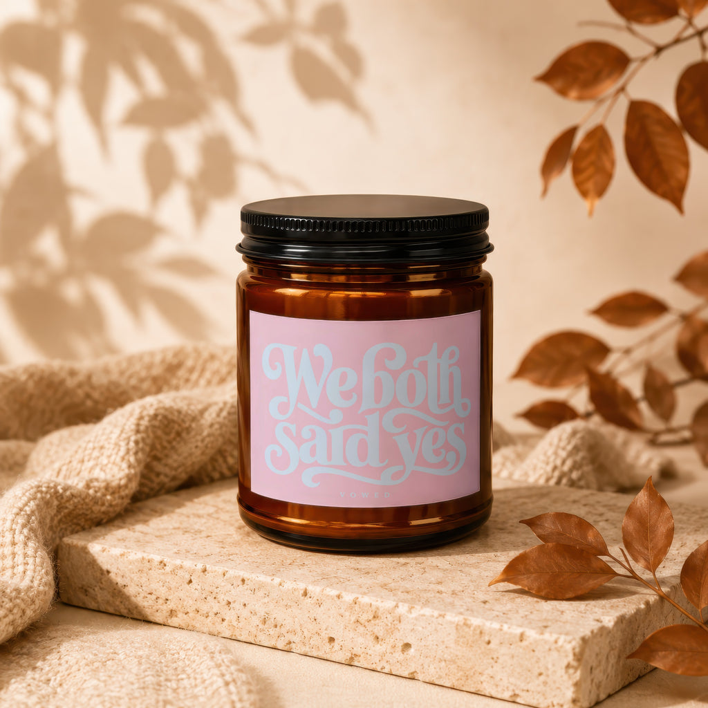 Amber candle with pink label that reads "We both said yes" and "vowed."