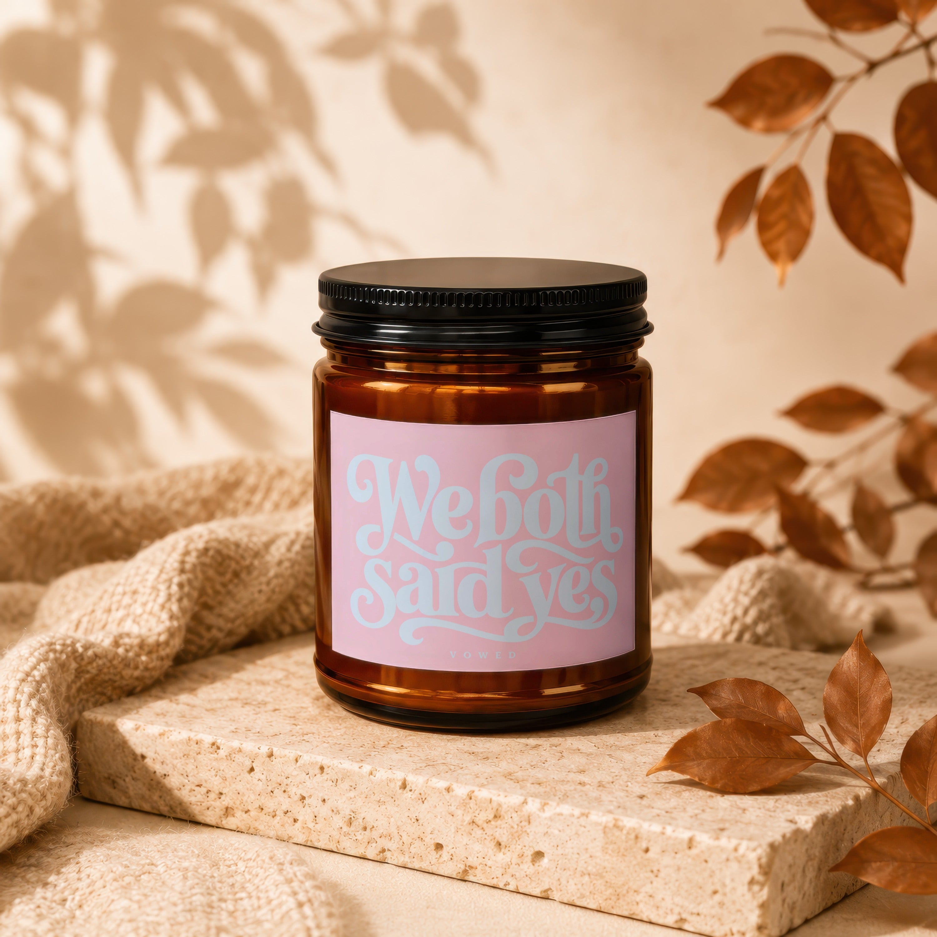 Amber candle with pink label that reads "We both said yes" and "vowed."