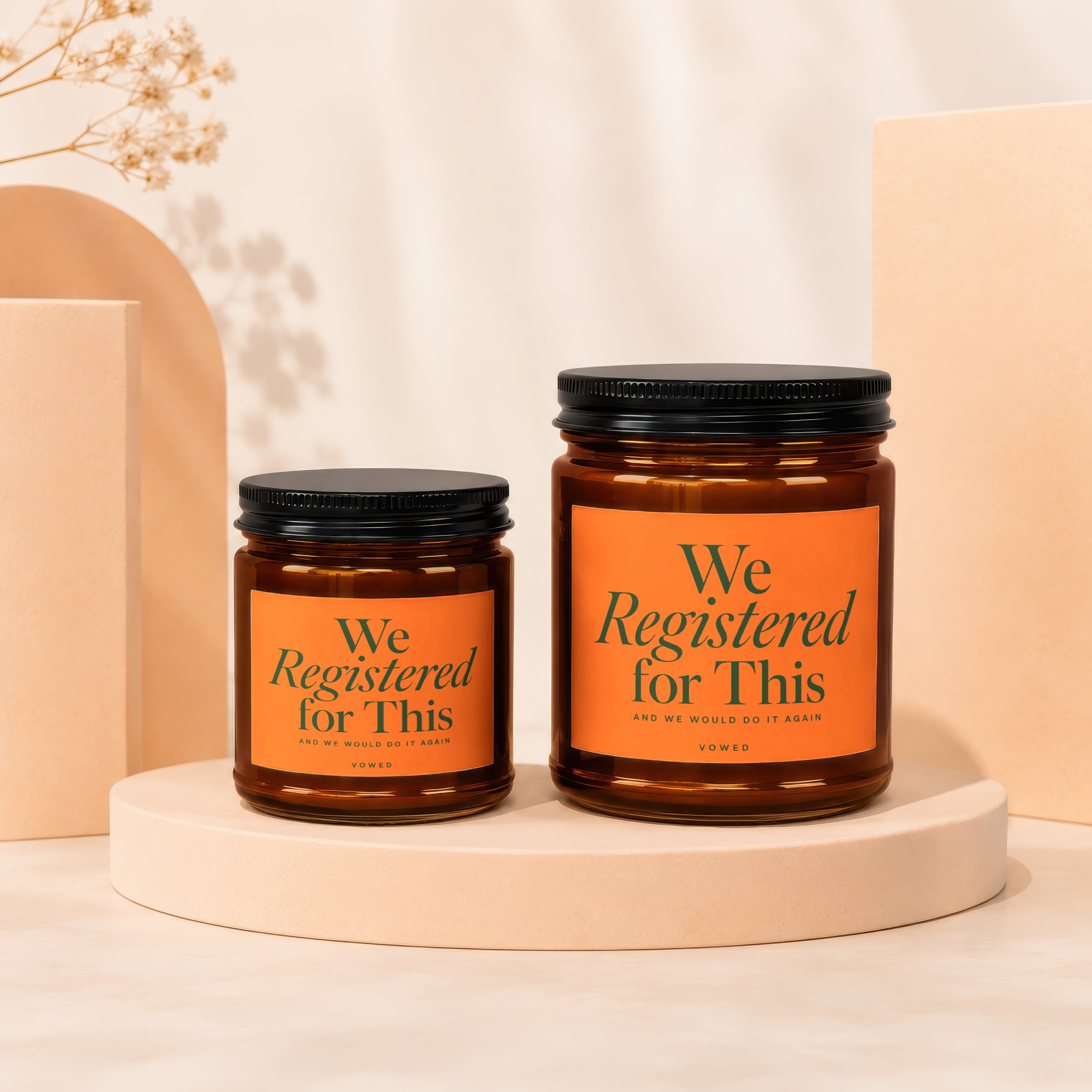 Two amber glass candles with orange labels reading "We Registered for This."