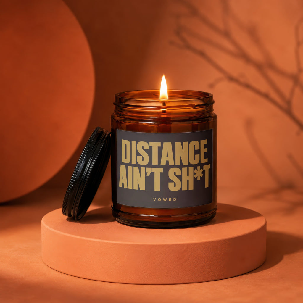 Amber jar candle with lit flame and text "DISTANCE AIN'T SH*T VOWED".