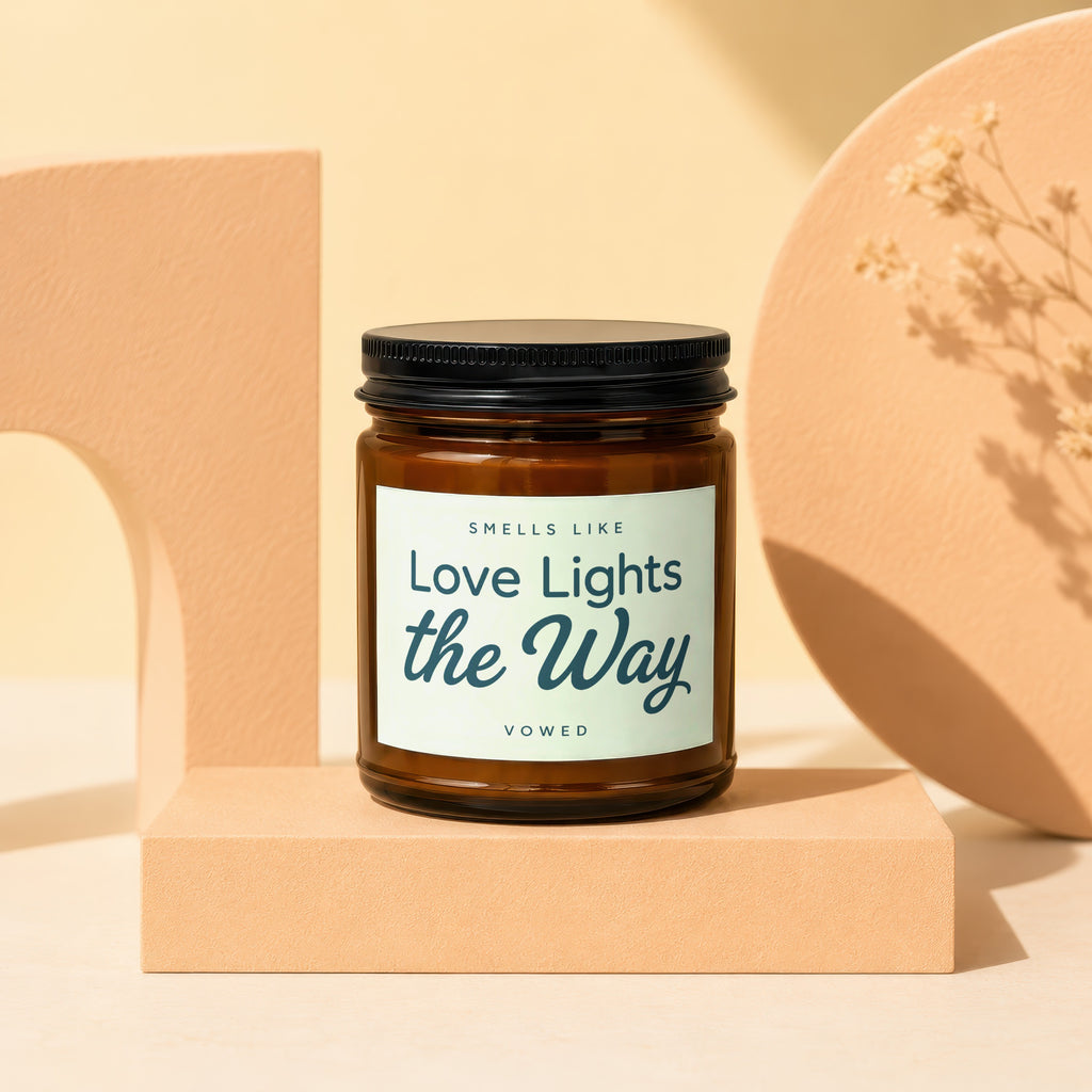 Amber candle with black lid reading "Smells Like Love Lights the Way Vowed".
