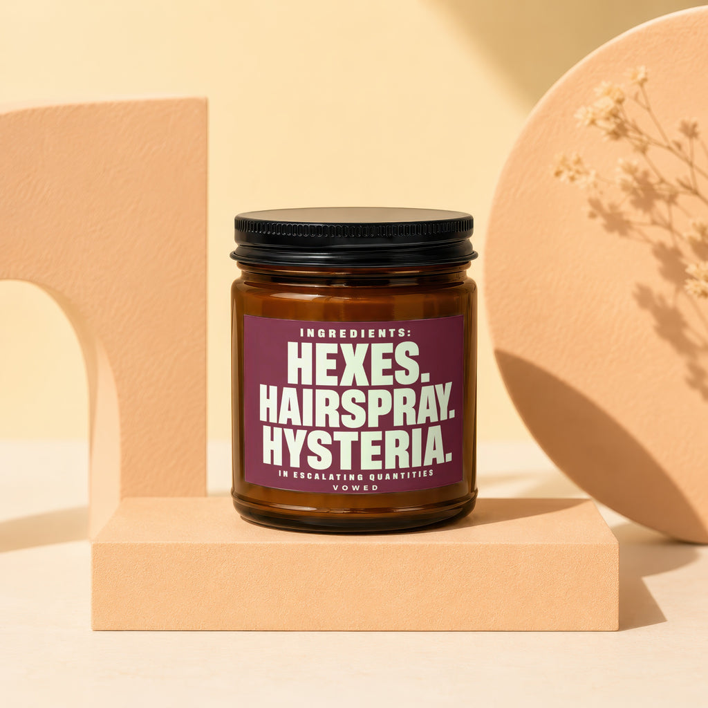 Brown jar with black lid on display pedestal, showing "Hexes. Hairspray. Hysteria." text.