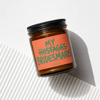 Amber jar candle with "MY HOSTAGES BRIDESMAIDS" text on an orange label.