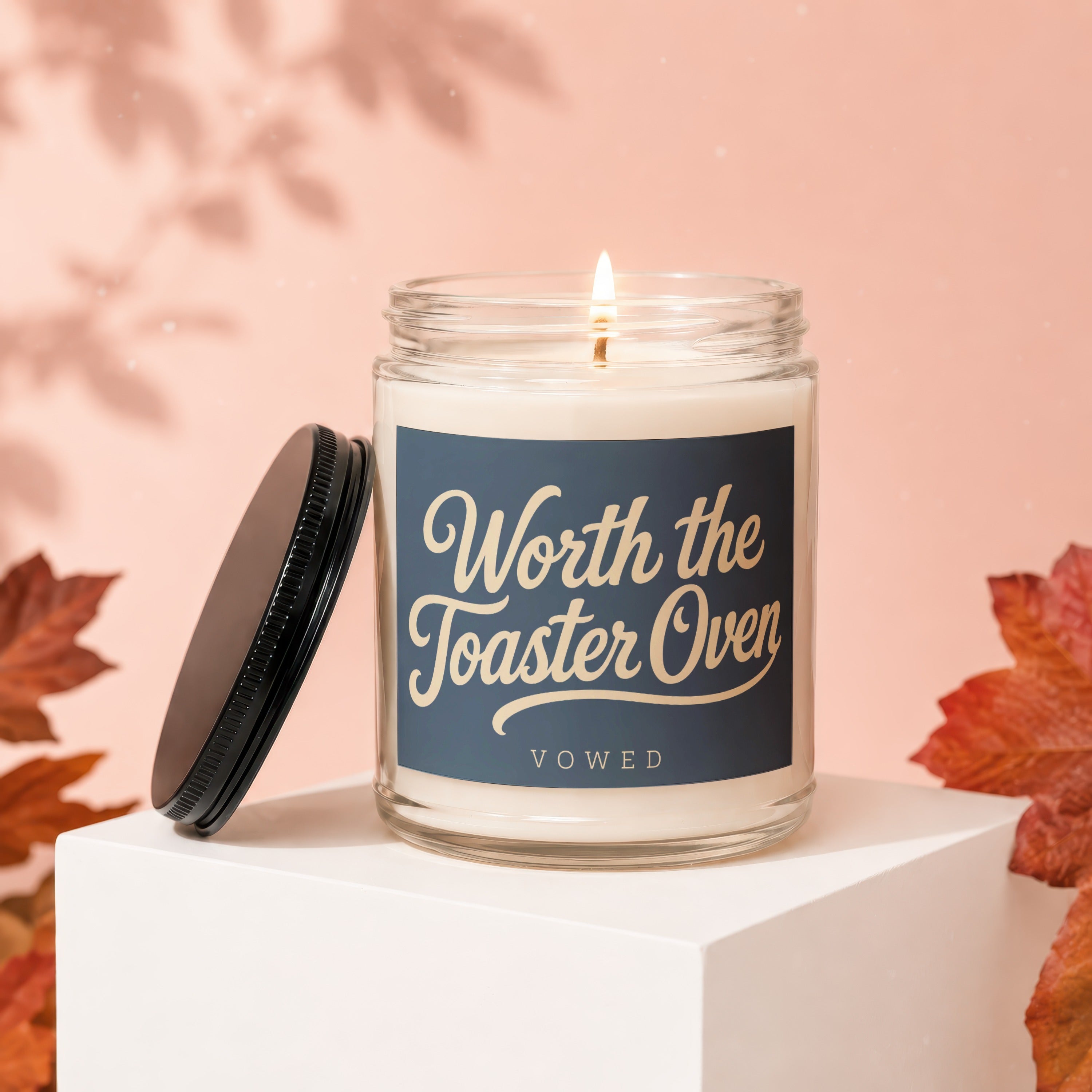 Lit candle in glass jar with navy label reading "Worth the Toaster Oven VOWED".