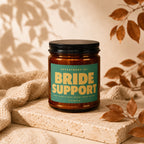 Brown glass candle jar with label reading "BRIDE SUPPORT" and "VOWED".