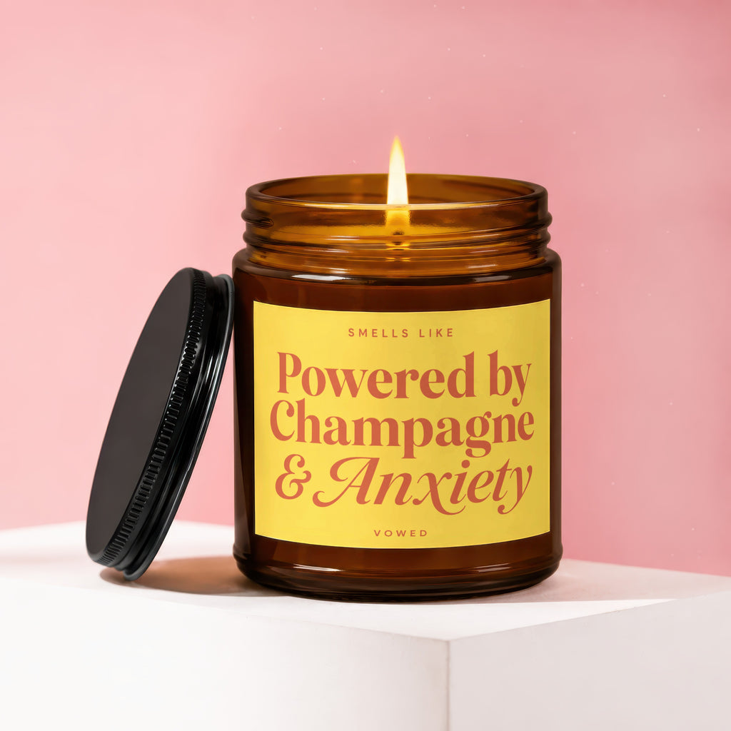 Amber jar candle with yellow label reading "Smells Like Powered by Champagne & Anxiety".