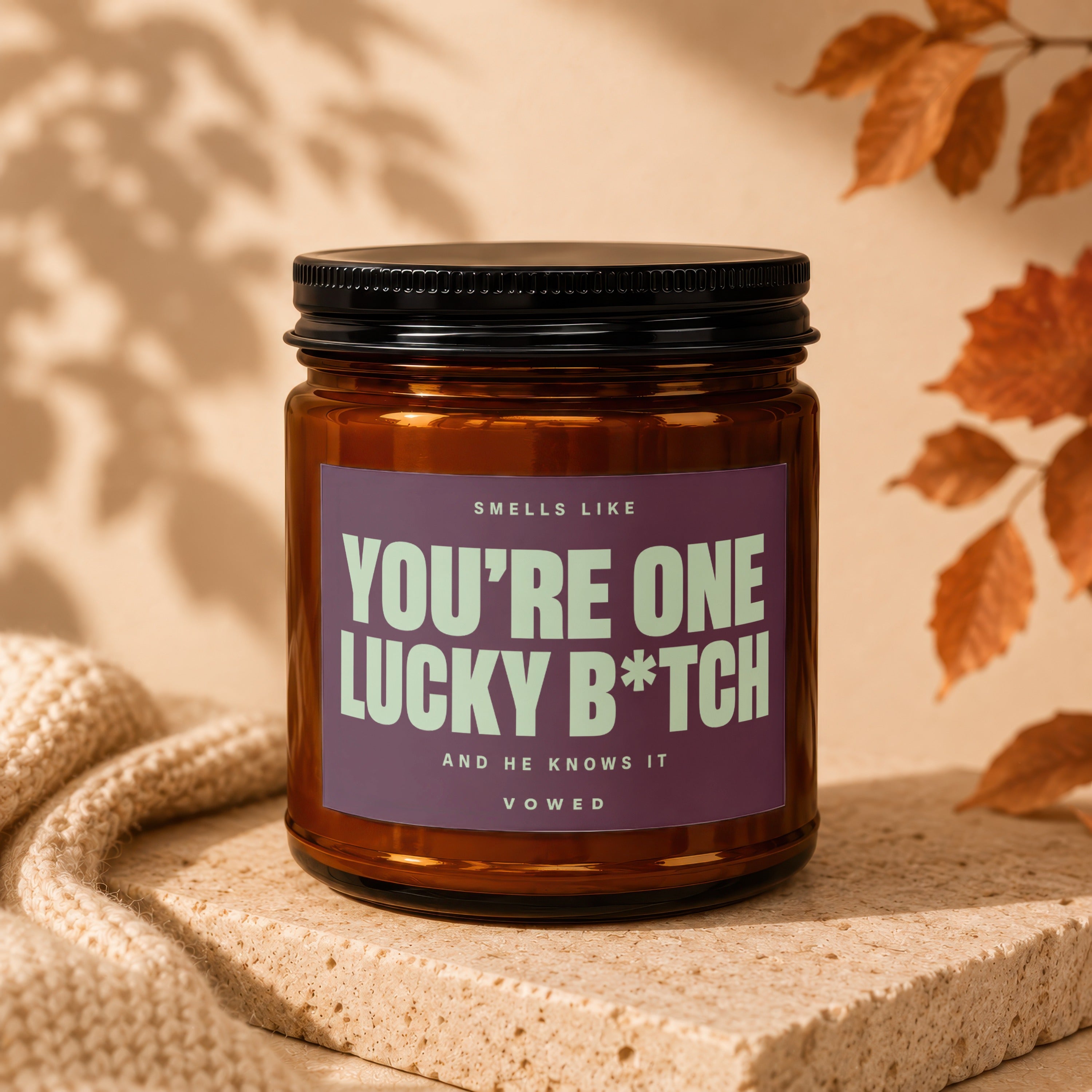 Brown glass candle with purple label reading "Smells like You're One Lucky B*tch".