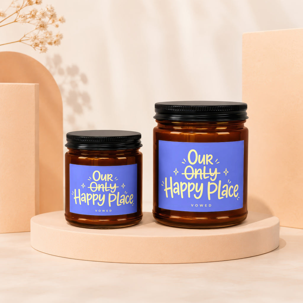 Two amber glass candles with black lids, displaying "Our Only Happy Place" on blue labels.