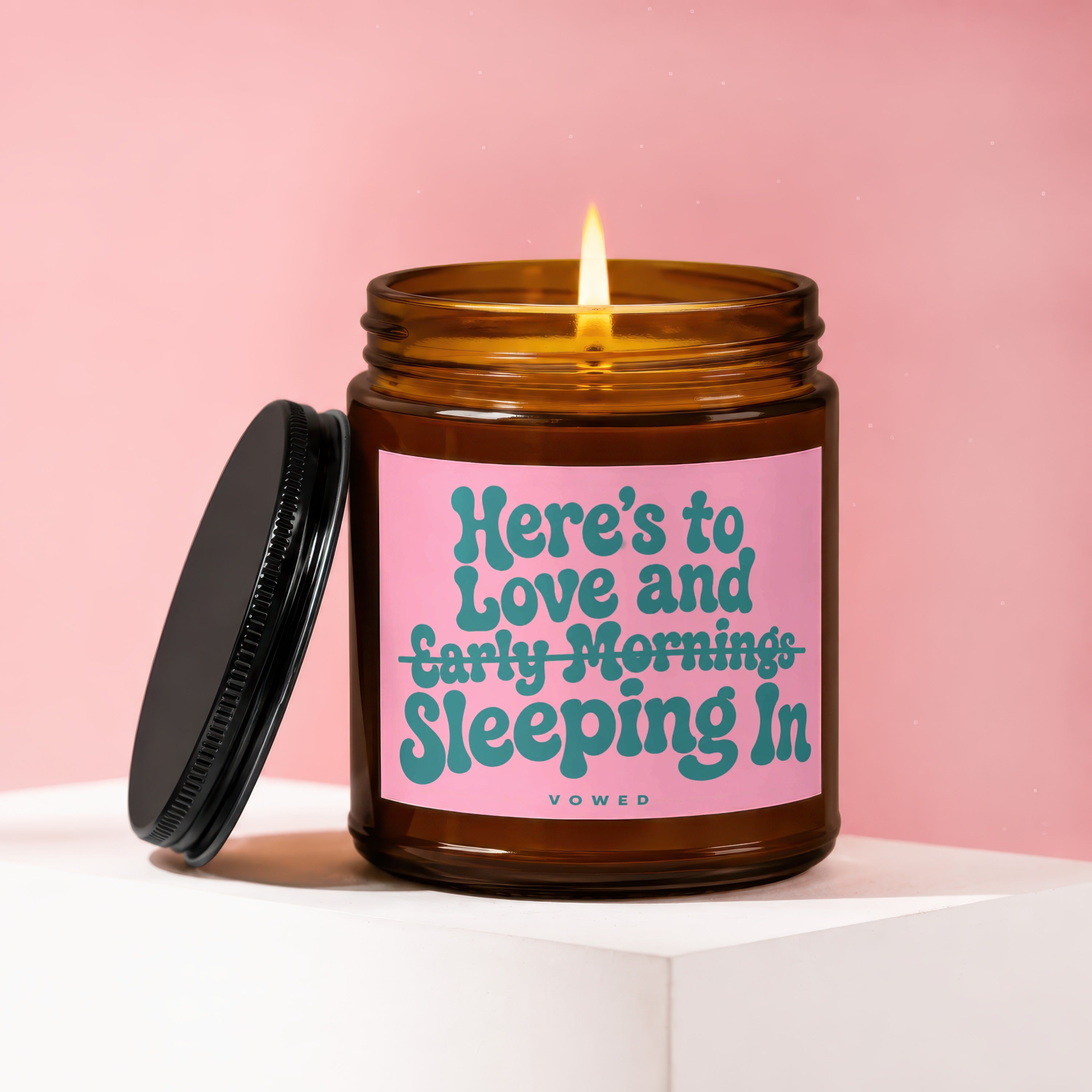 Amber jar candle with pink label reading "Here's to Love and Sleeping In Vowed."