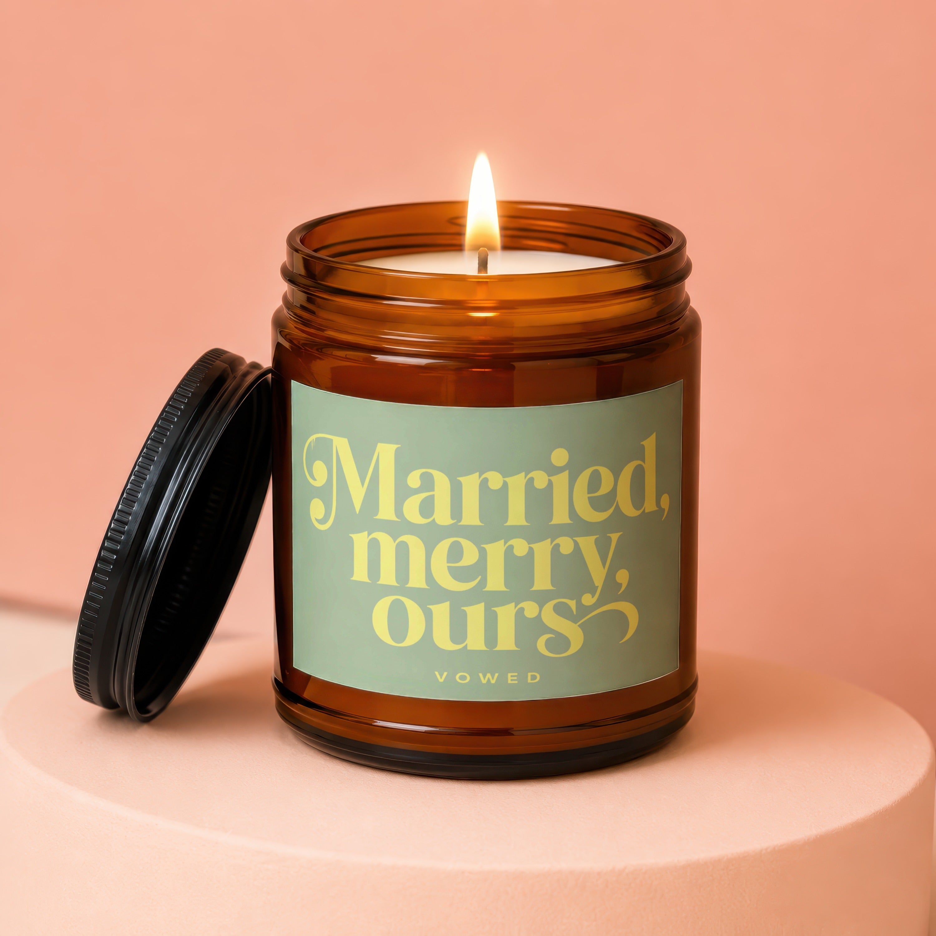 Amber glass candle with lit wick and black lid, labeled "Married, merry, ours, VOWED".