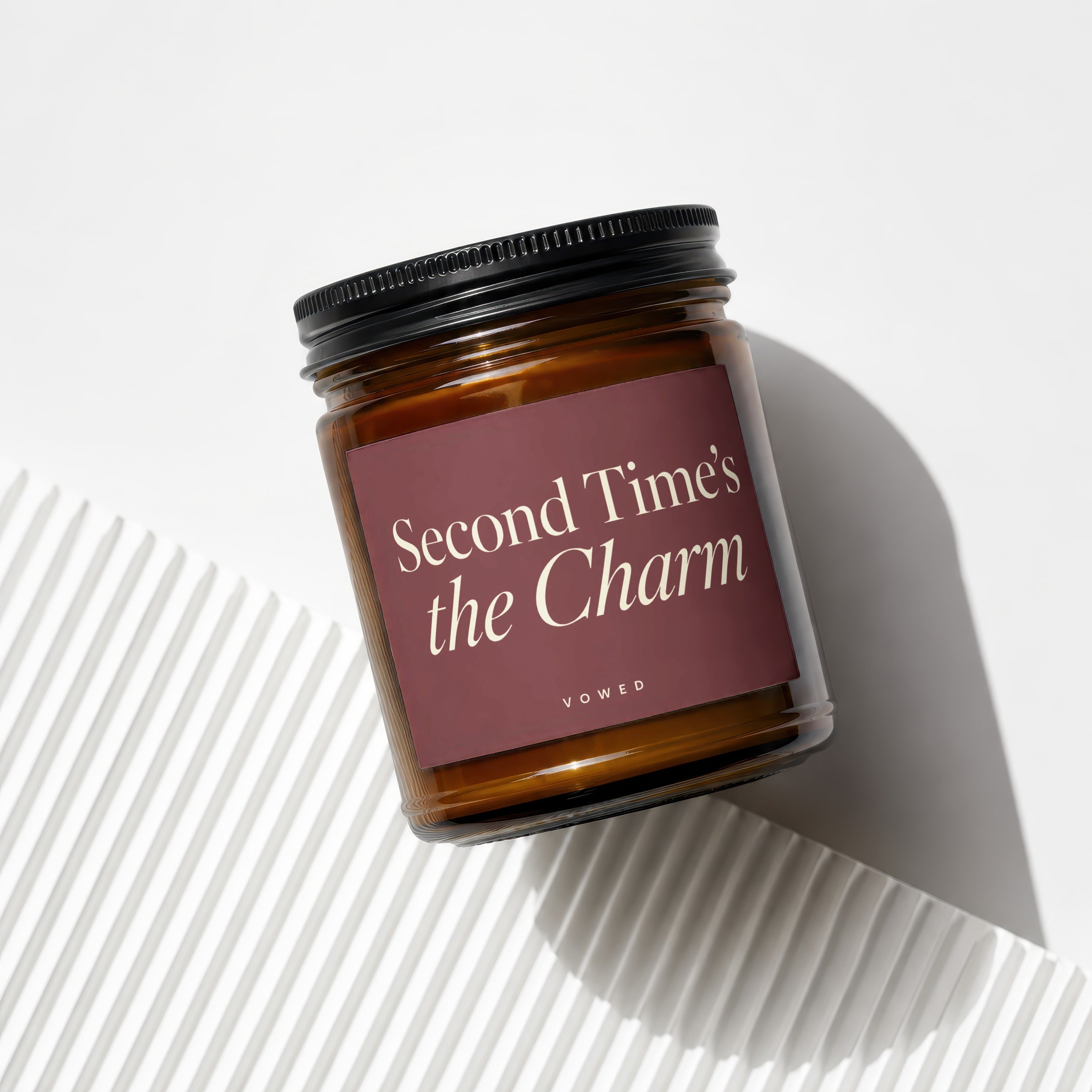 Glass candle jar with maroon label reading "Second Time's the Charm" and "VOWED".