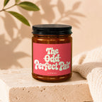 Amber jar candle with pink label reading "The Odd Perfect Pair Vowed".
