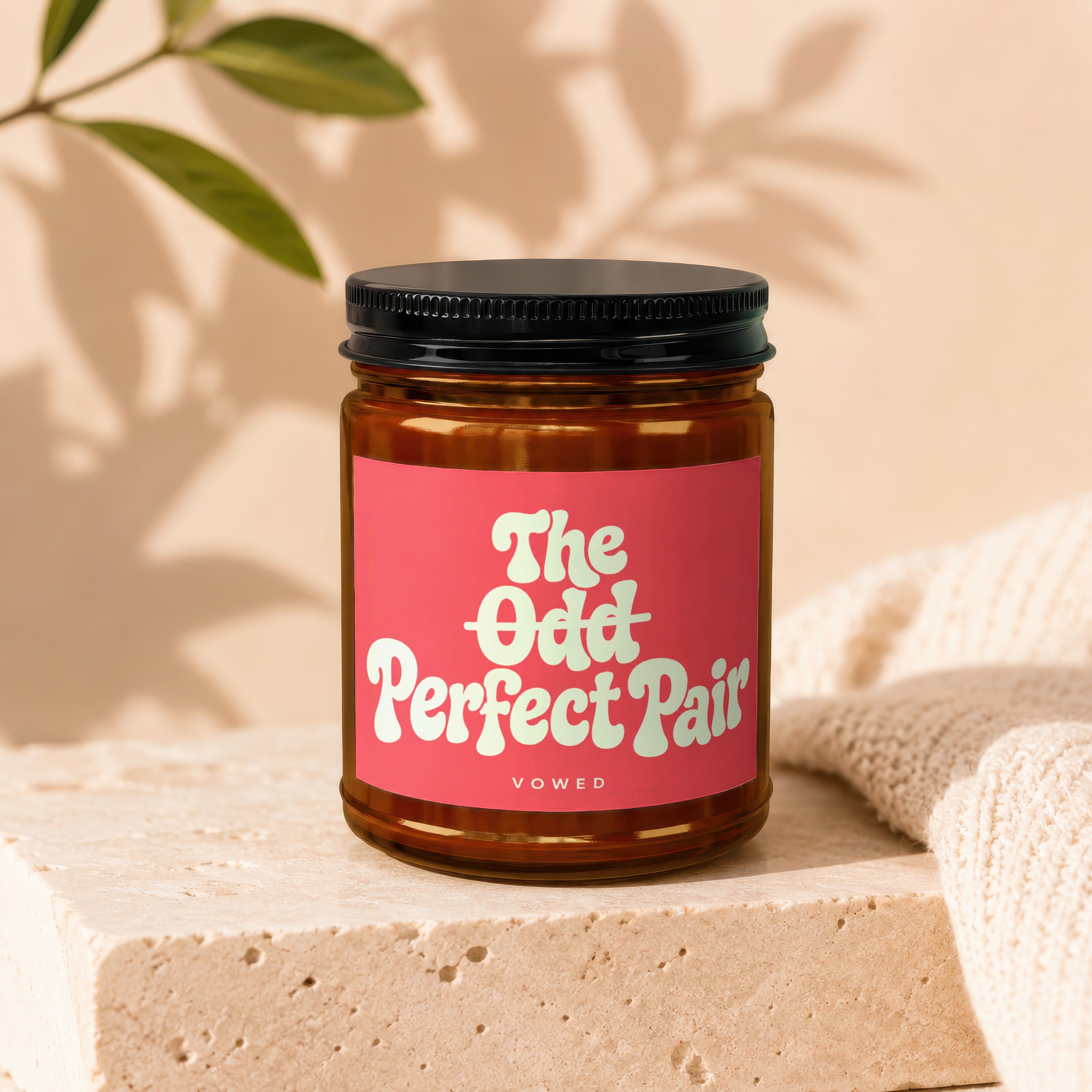 Amber jar candle with pink label reading "The Odd Perfect Pair Vowed".