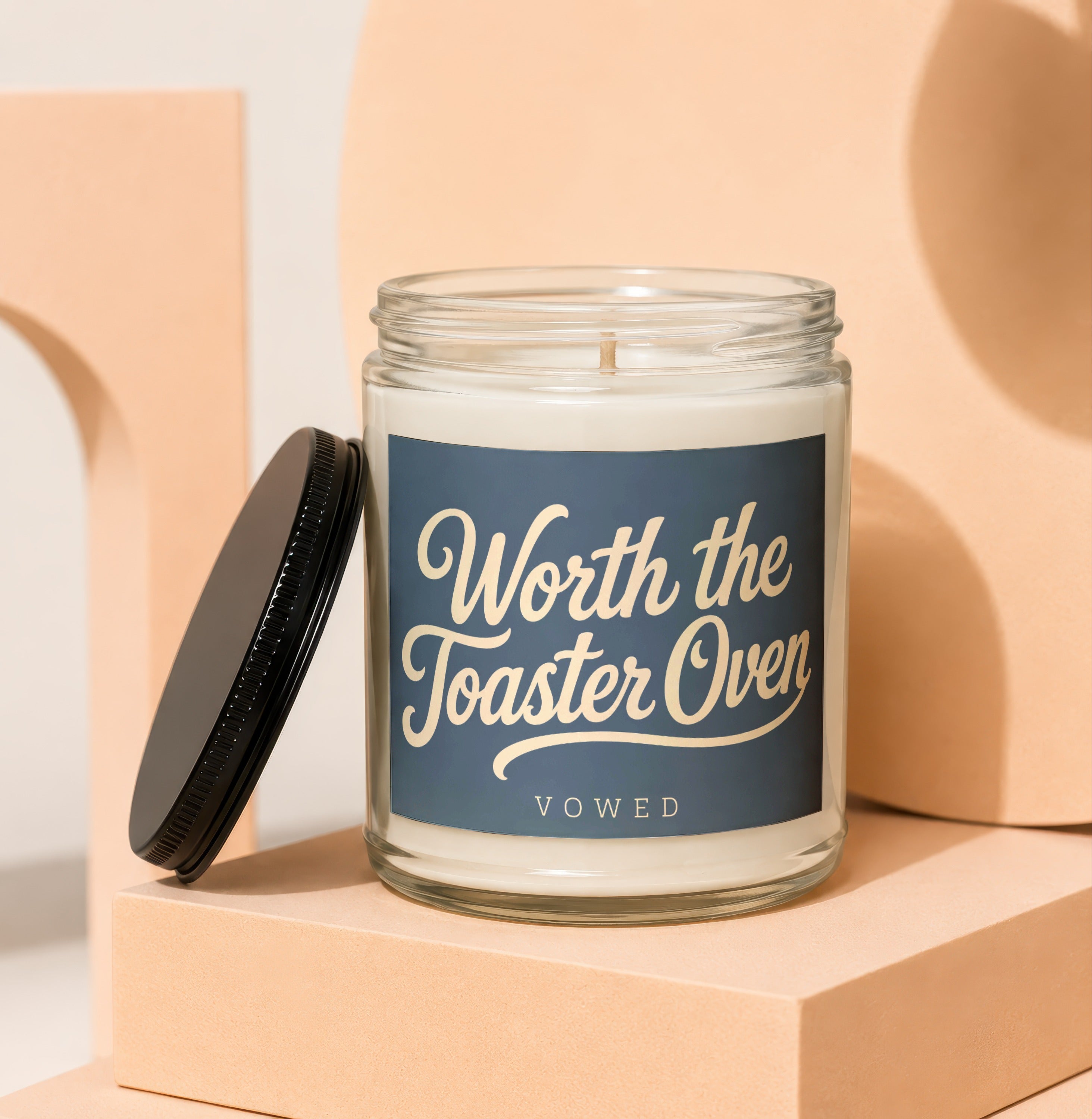 Glass candle with dark blue label that reads "Worth the Toaster Oven VOWED".