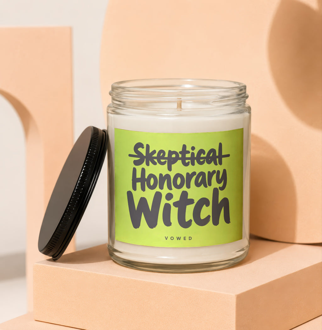 Glass candle with green label reading "Skeptical Honorary Witch Vowed."