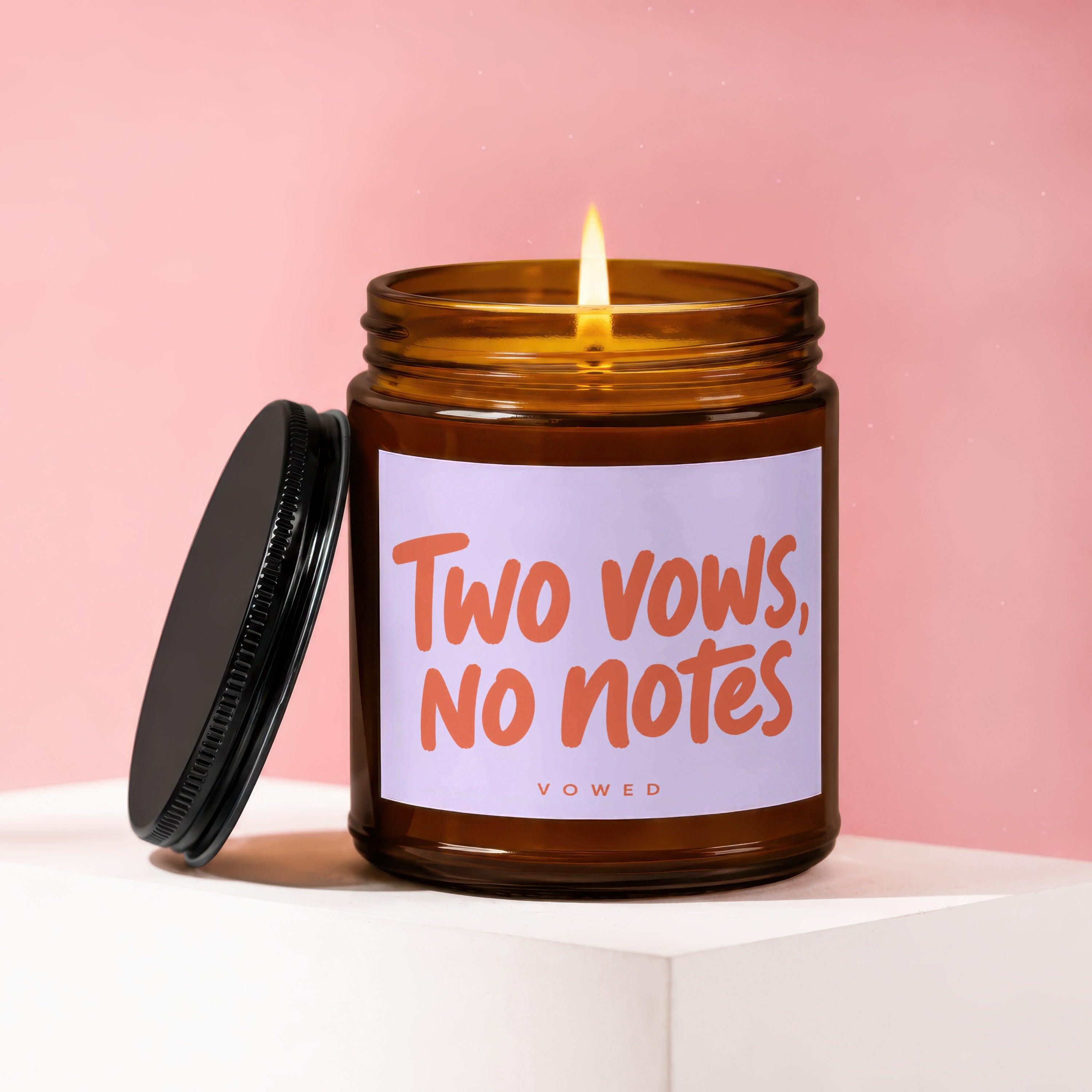 Amber glass candle with lit flame and label reading "Two vows, no notes".