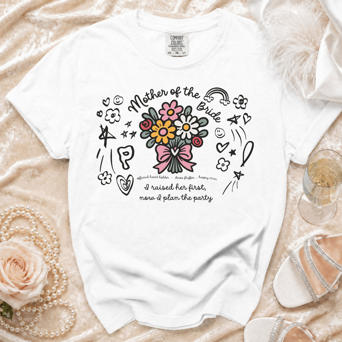 White t-shirt with "Mother of the Bride" text and floral design, saying "I raised her first, now I plan the party."