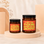Two amber glass candles with orange labels reading "Smells like I hit the f*cking mother-in-law jackpot".