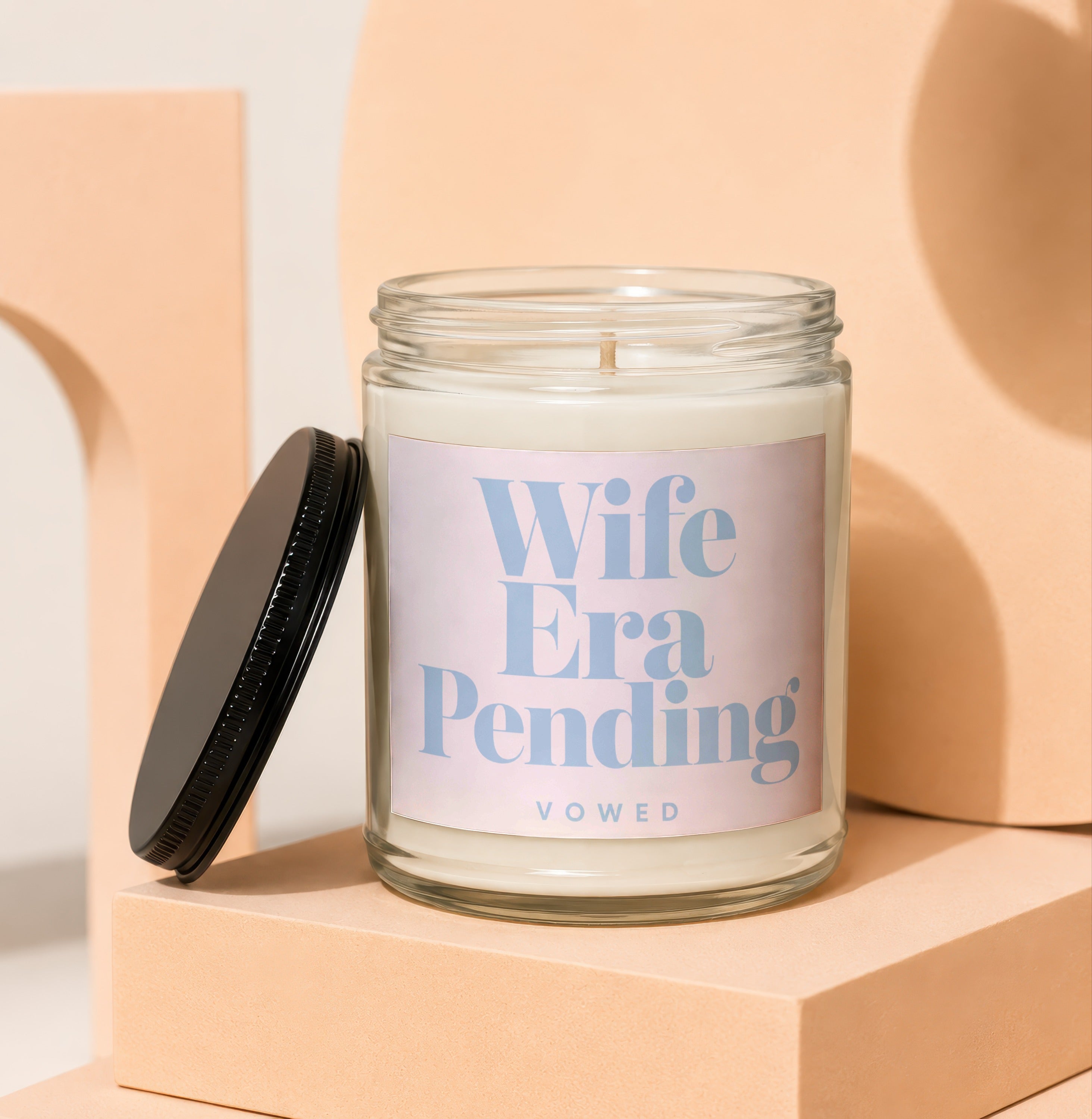 Glass candle labeled "Wife Era Pending VOWED" with black lid removed.