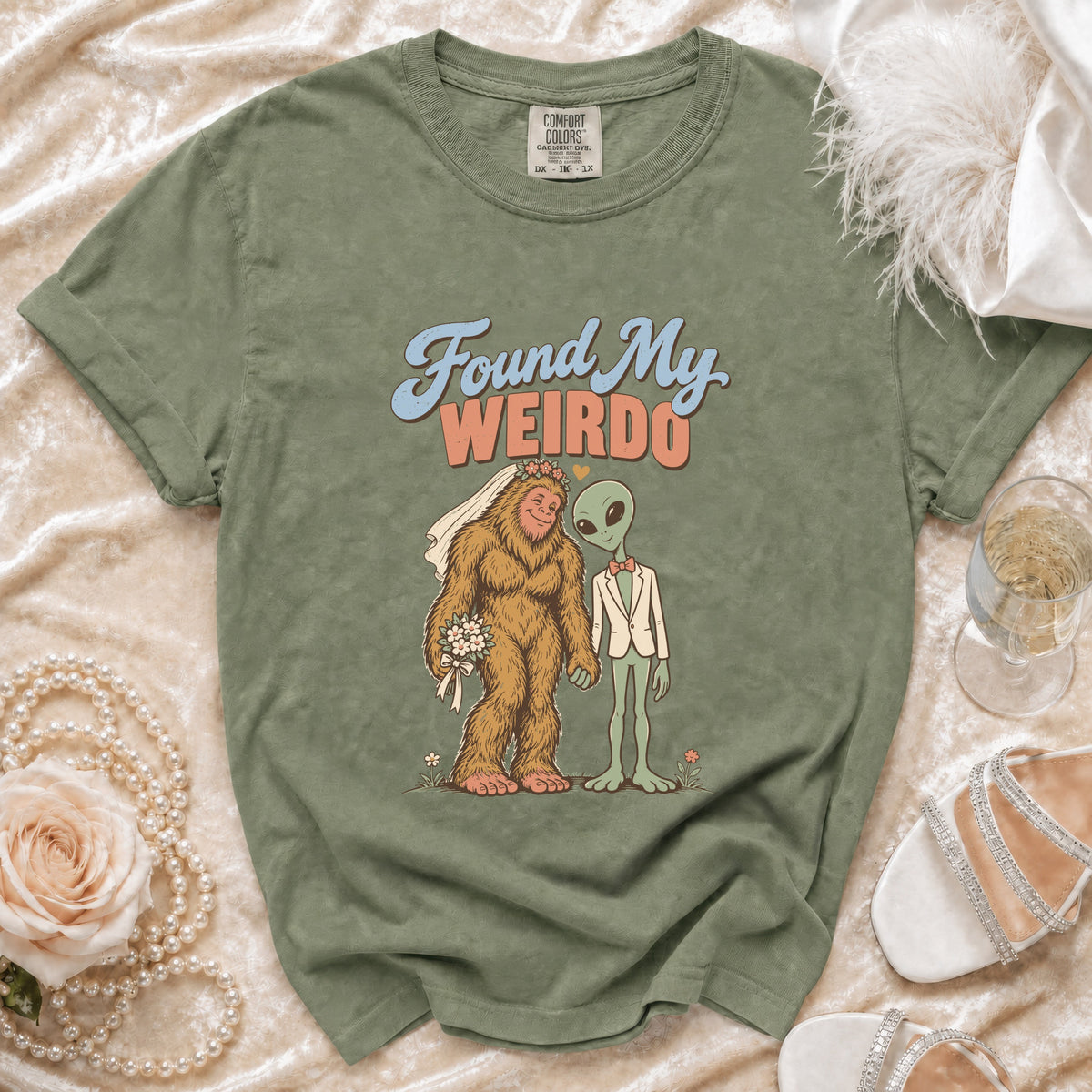 Green t-shirt with Bigfoot in a wedding veil and alien in a suit saying "Found My Weirdo."