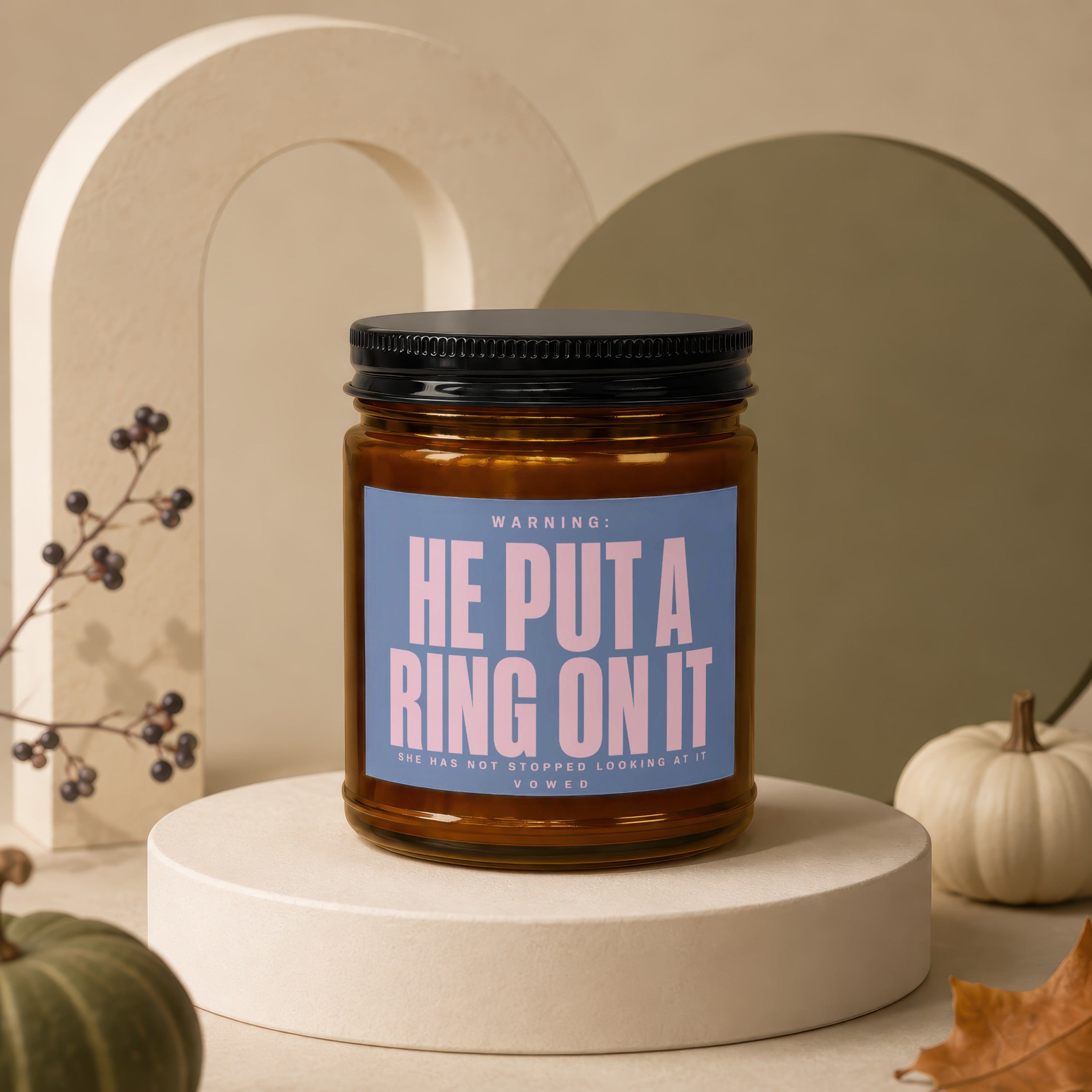 Amber candle with black lid, label reads "HE PUT A RING ON IT".