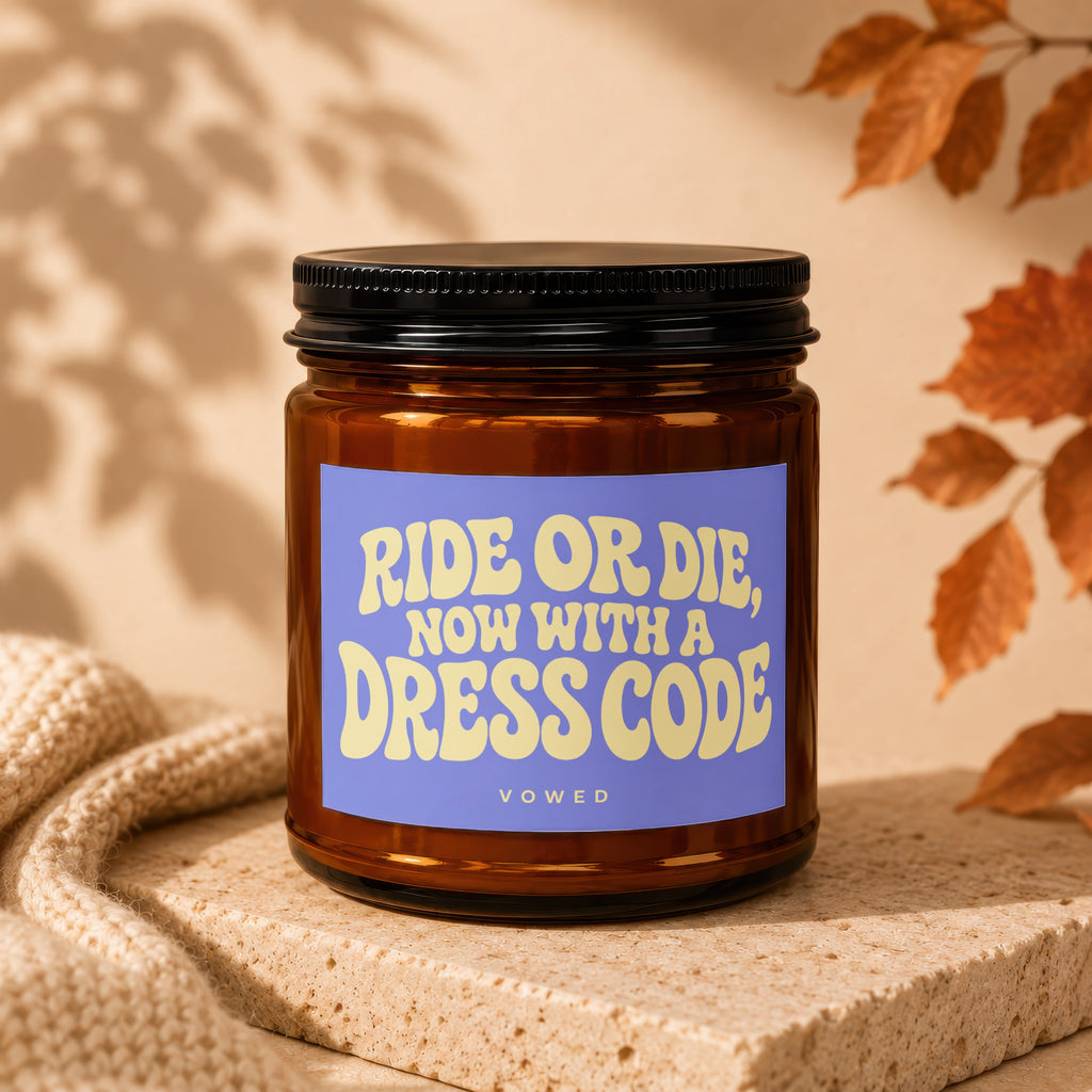 Brown glass candle with label reading "RIDE OR DIE, NOW WITH A DRESS CODE BOWED".