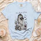 Light blue t-shirt with "This Bride Bites" graphic of bride at mirror with gothic elements.