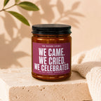 Amber jar candle with label reading "We came. We cried. We celebrated."