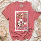 T-shirt with pink stamp design featuring cowboy boots, "Reckless in Texas", and "Olivia's Bach".