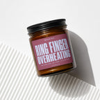 Amber glass candle with maroon label warning "RING FINGER OVERHEATING".