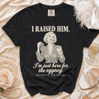 Black t-shirt featuring a graphic illustration of a woman holding mistletoe and eggnog with text reading I RAISED HIM. I'm just here for the eggnog. MOTHER OF THE GROOM.