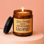 Amber jar candle labeled "Two Hearts, One Mortgage Home" with a lit flame.