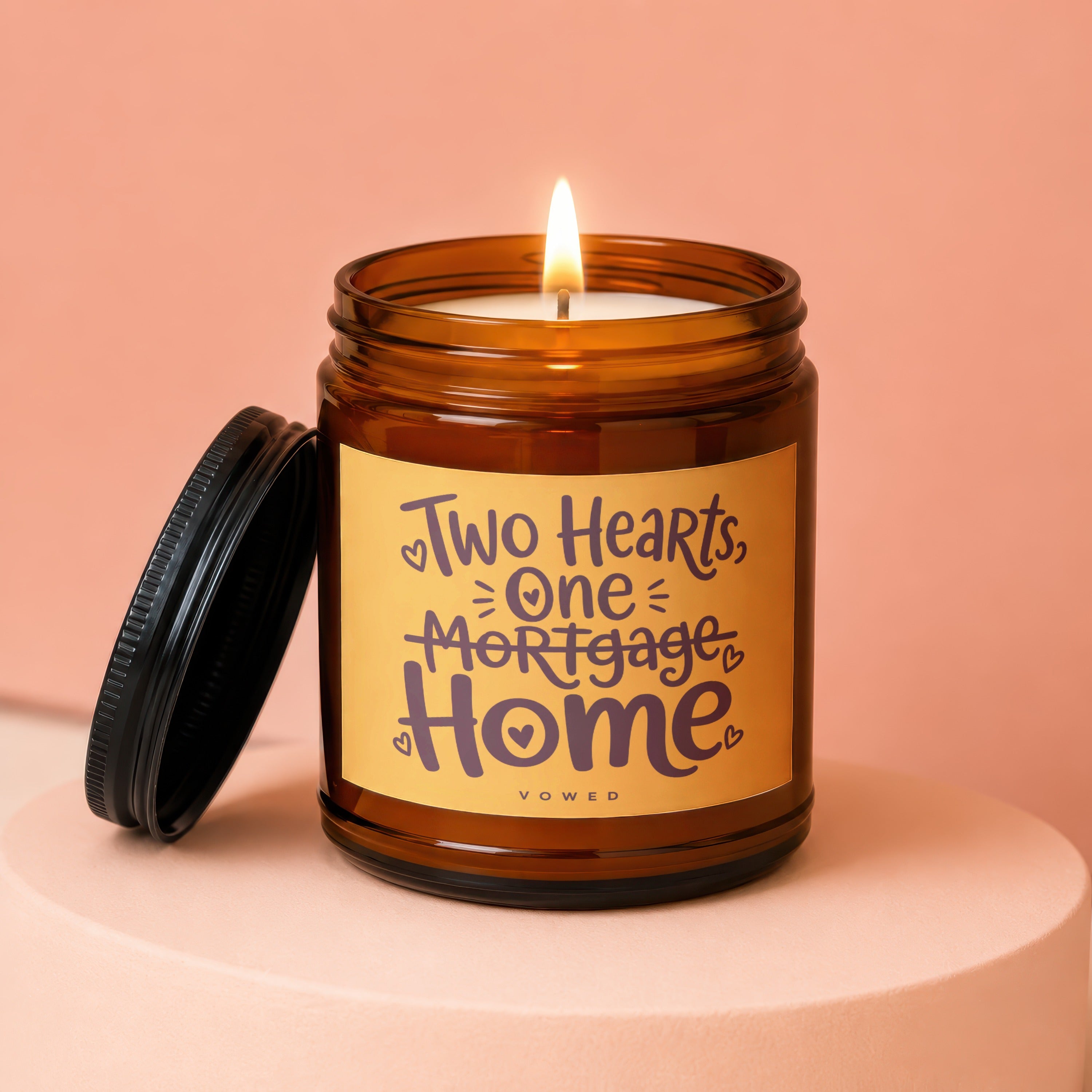 Amber jar candle labeled "Two Hearts, One Mortgage Home" with a lit flame.