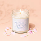 Glass jar candle with text "Keeping It Together... Mostly. Vowed" among pink petals.