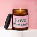 Amber glass candle with lit wick and black lid, "Love That Lasts" text.
