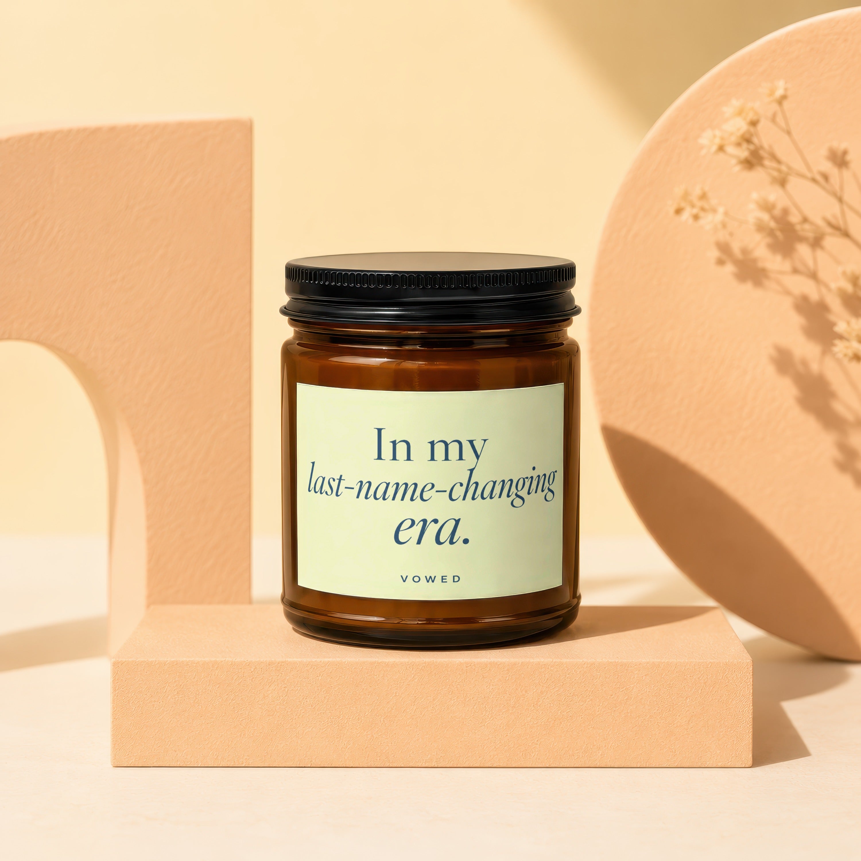 Amber glass candle with black lid, labeled "In my last-name-changing era. VOWED".