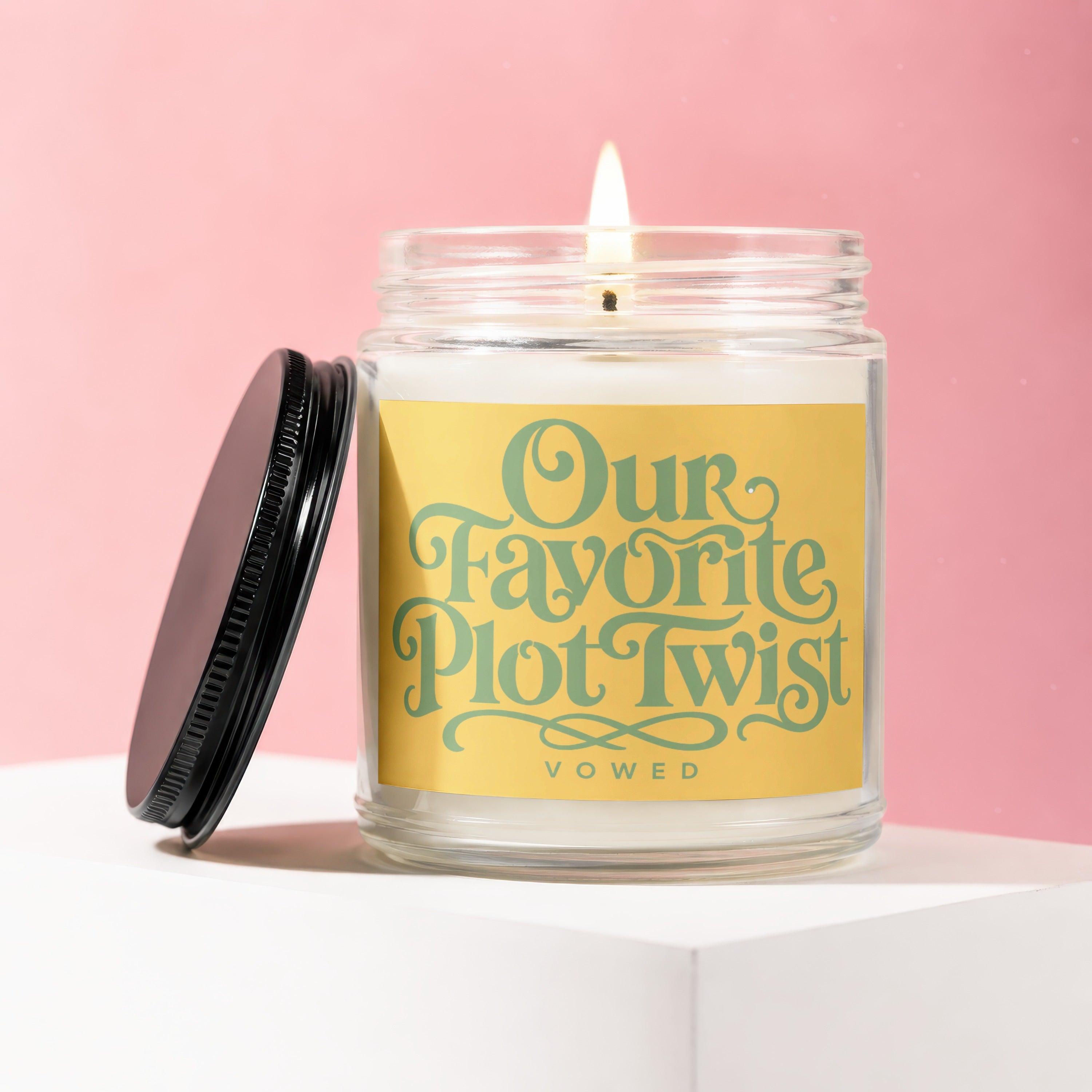 Lit candle in a glass jar with a yellow label reading "Our Favorite Plot Twist" and "vowed".