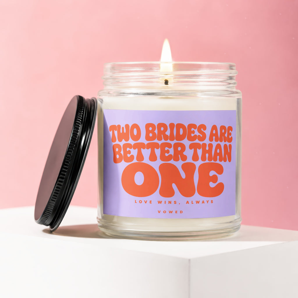 Candle with text "TWO BRIDES ARE BETTER THAN ONE LOVE WINS, ALWAYS VOWED" on a pink background.
