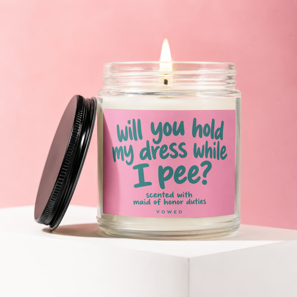 Candle with pink label reading "Will you hold my dress while I pee?"