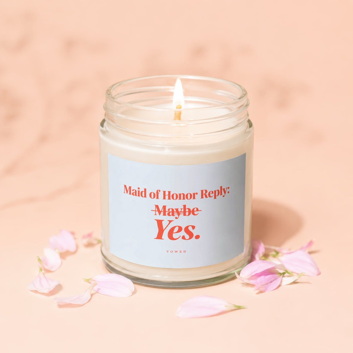 Lit candle with label "Maid of Honor Reply: Maybe Yes. VOWED" surrounded by petals.